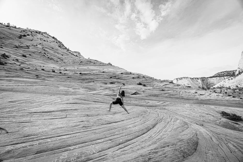 A focused woman in a warrior yoga pose on a rock under a clear sky